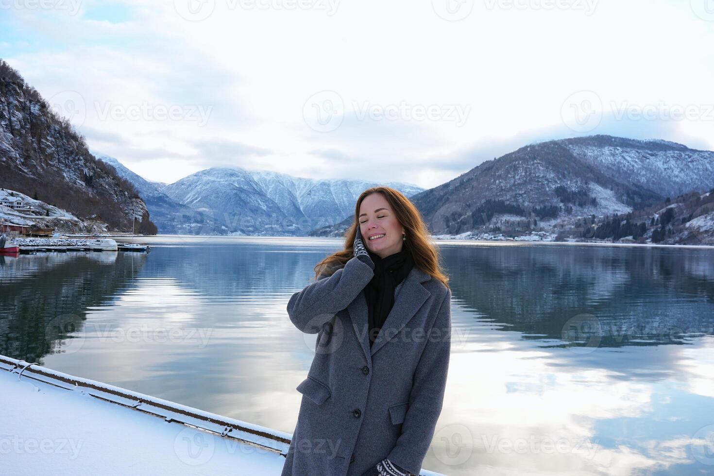 Smiling woman by snowy fjord and mountains in Gaupne, Norway winter scene photo