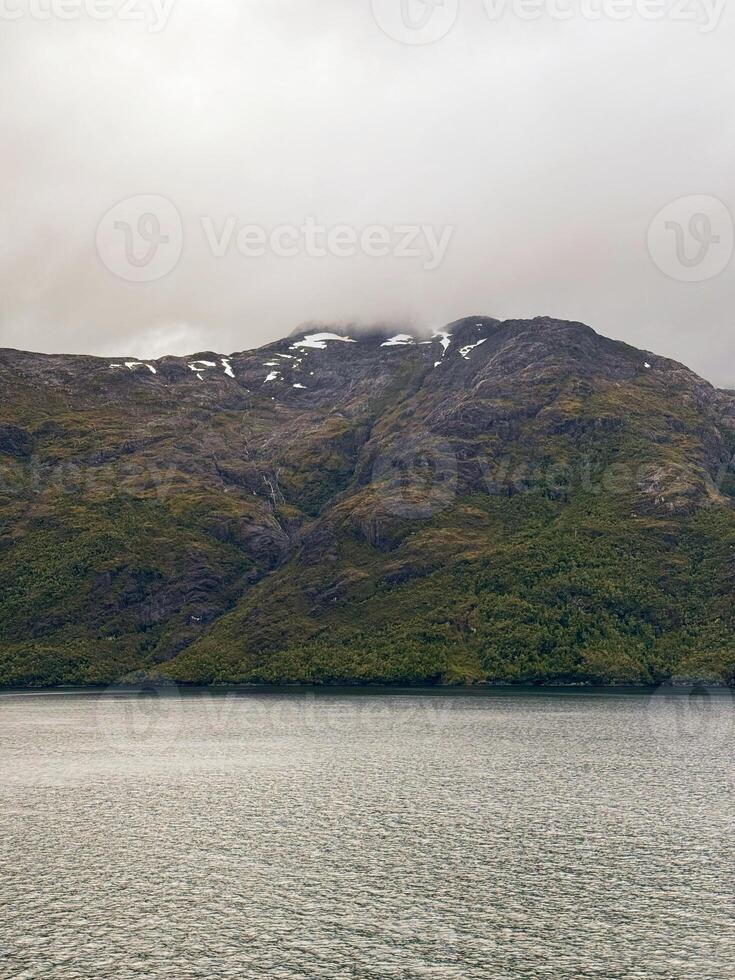 Cloudy Mountain Landscape with Snow Patches Above Calm Fjord Waters photo