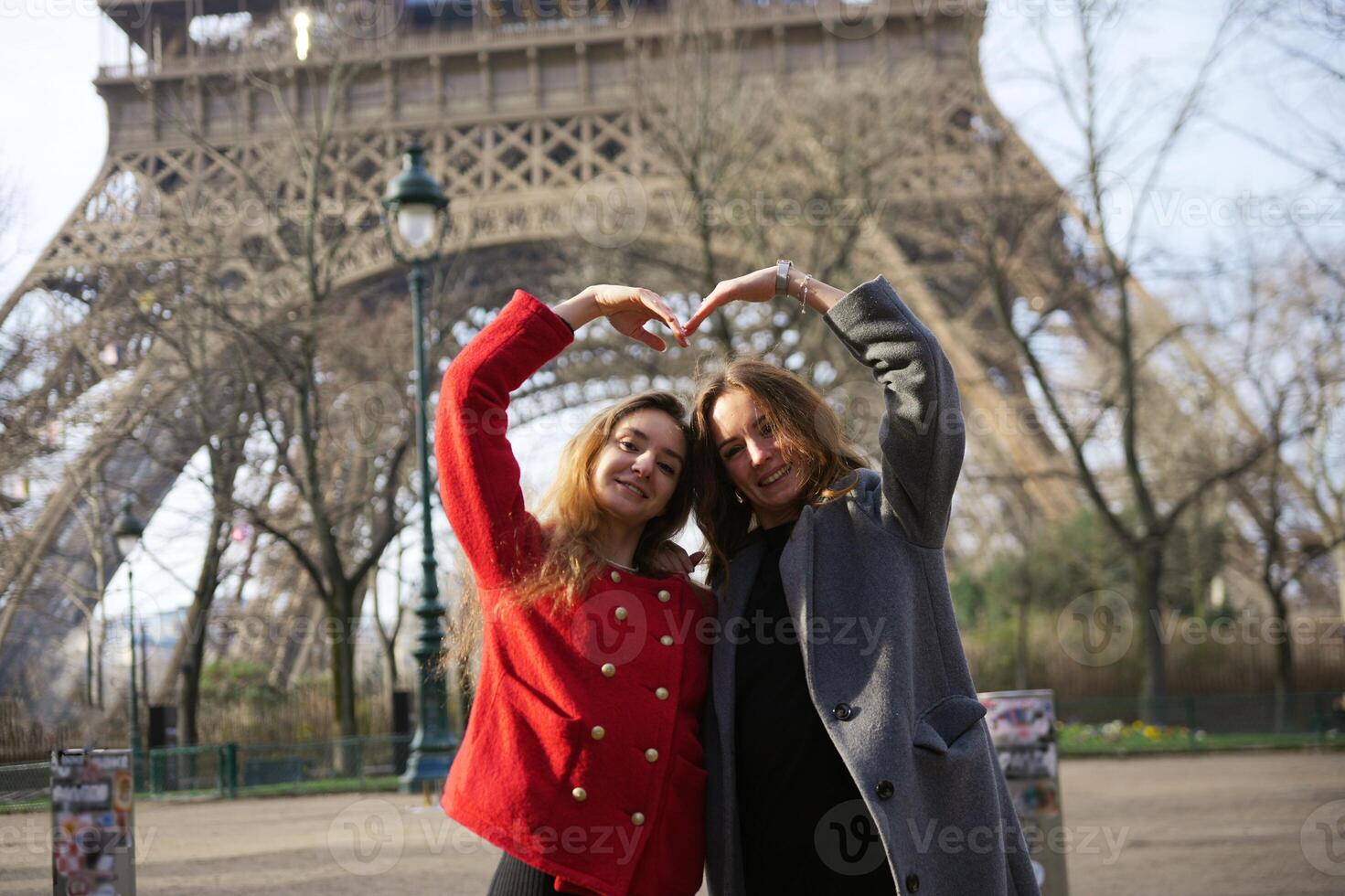 Two friends forming heart shape in front of Eiffel Tower photo