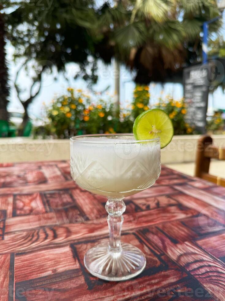 Pisco Sour Cocktail with Lime Garnish on Outdoor Table in Sunny Garden Cafe photo
