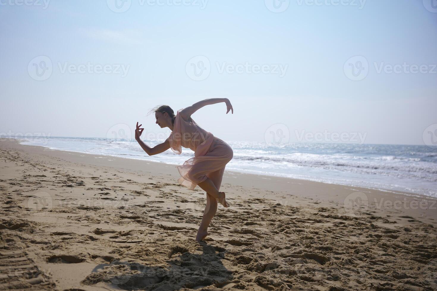 Dancer in motion on wide sandy beach under bright sky near ocean waves photo