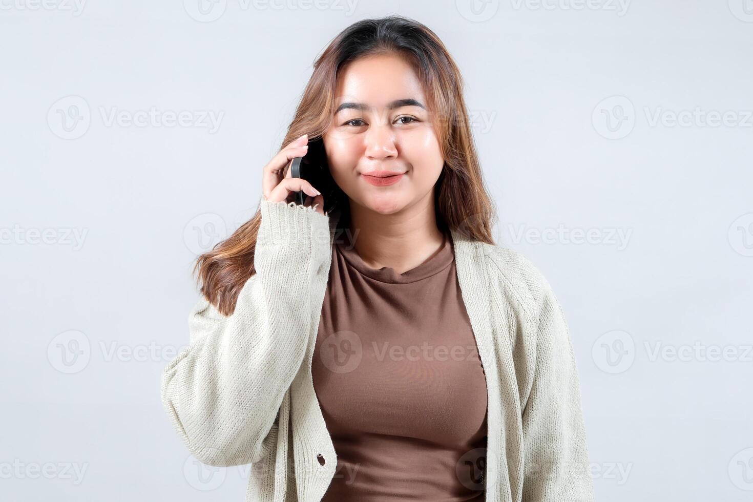 A young woman in a cozy sweater smiles while talking on her mobile phone, conveying connection and communication against a gray background photo