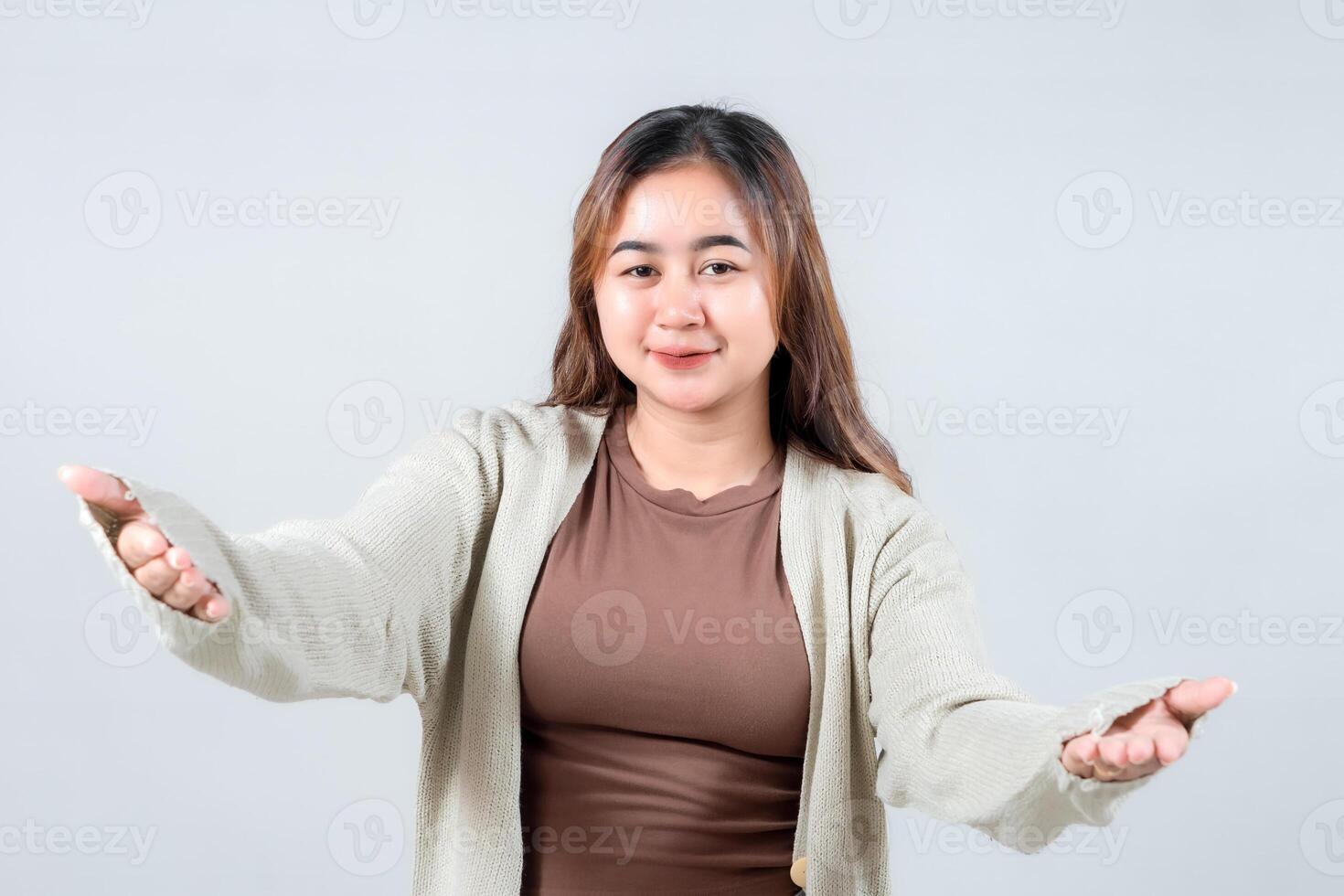 A joyful woman in a cozy sweater opens her arms for a hug, expressing warmth, welcome, and affection against a neutral background. photo
