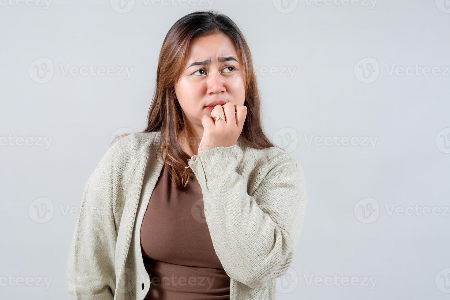 A young woman with long hair looks conacerned while biting her nails wering a cozy sweater. Her expression reflects anxiety and contemplation capturing a relatable moment photo