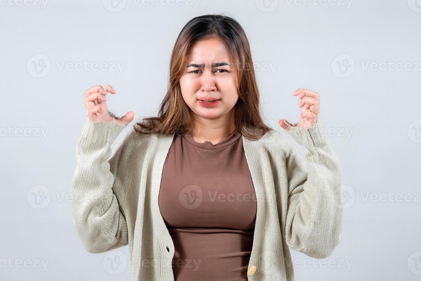 A young woman expresses frustration or annoyance, her face scrunched up and hands gesturing. Wearing a cozy sweater, she conveys a clear message of displeasure against a gray background. photo