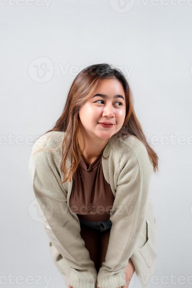 A young woman in a cozy sweater leans forward with a curious and playful expression, looking to the side against a neutral background photo