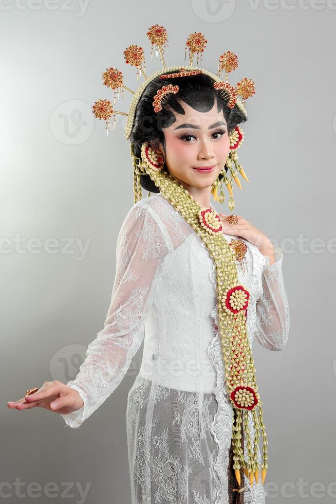 A Indonesian bride in Solo Putri attire wearing a golden headdress, jasmine garlands, and a white lace kebaya. She radiates grace and elegance with a soft, confident smile. photo