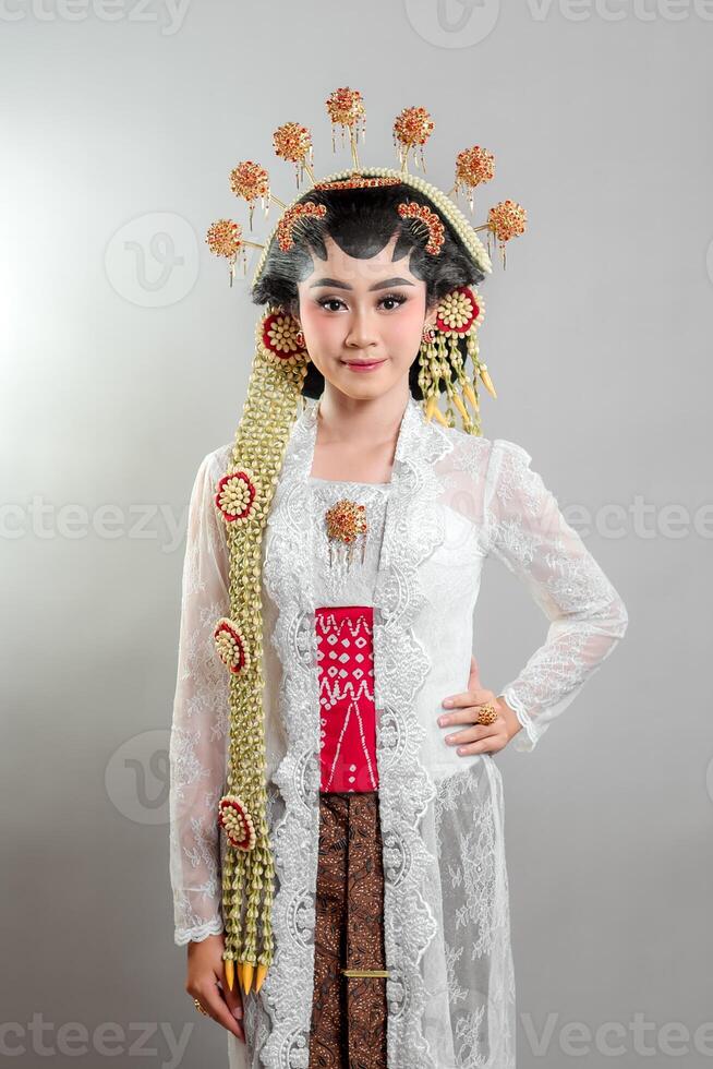An Indonesian bride in Solo Putri attire, wearing a golden and jasmine headdress, white lace kebaya, and batik, smiling gently with a graceful and confident expression. photo