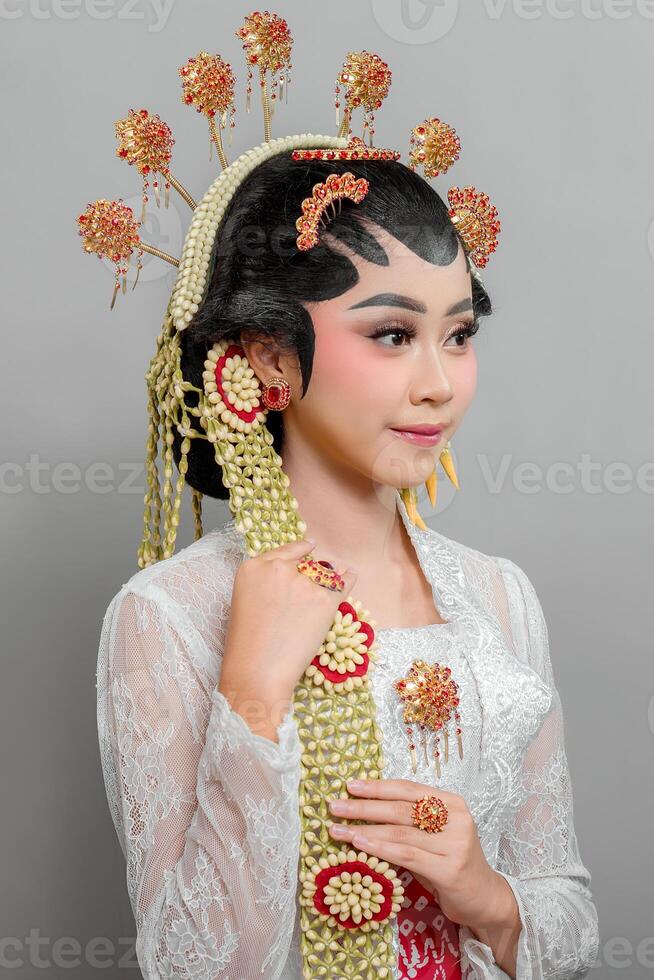Indonesian bride in Solo Putri traditional attire wearing an ornate golden headdress, jasmine accessories, and an elegant lace kebaya. She smiles gracefully, exuding cultural beauty. photo
