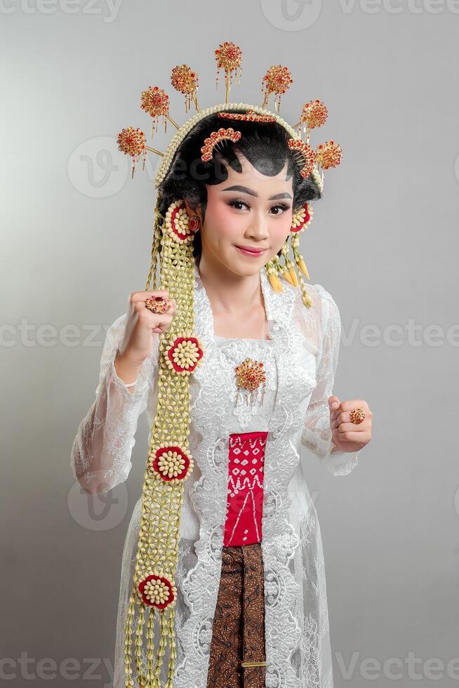 Indonesian bride in Solo Putri attire, wearing a golden headdress and jasmine garland. She poses with a gentle smile and a raised fist, symbolizing confidence, elegance, and cultural pride photo