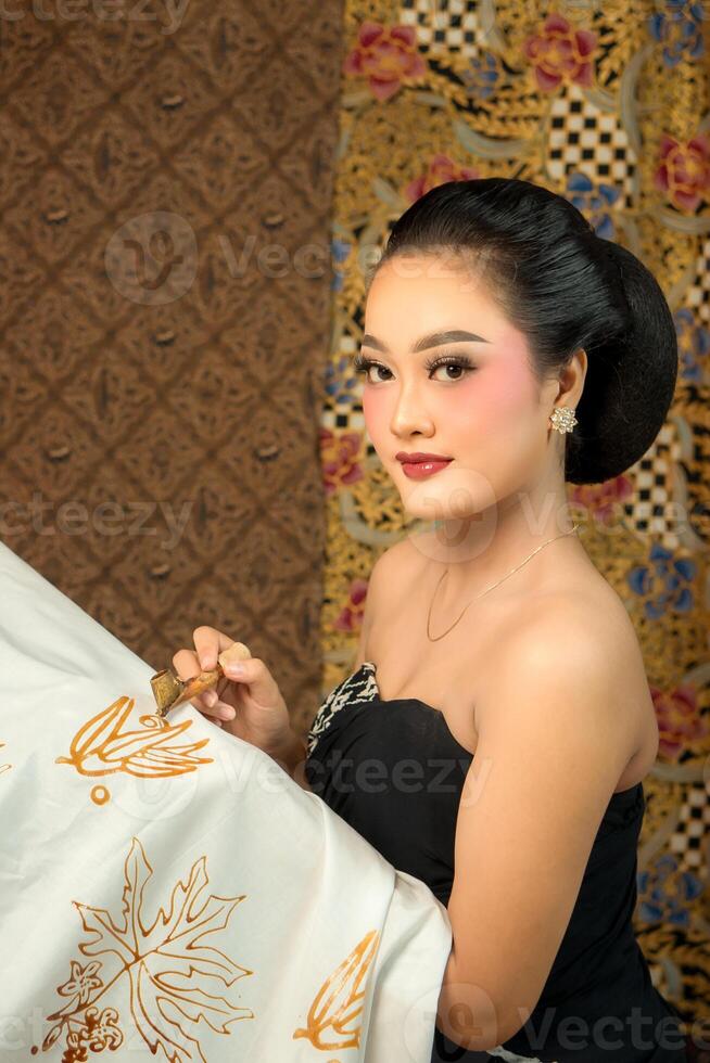 Indonesian woman creating batik with a canting, wearing traditional attire. Elegant look, rich cultural heritage, and intricate patterns. Artistic craftsmanship of Southeast Asian textile art photo