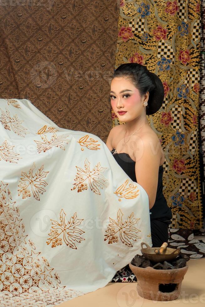 An Indonesian woman poses with batik fabric, showcasing her intricate design work with delicate patterns, representing traditional craftsmanship and cultural artistry. photo