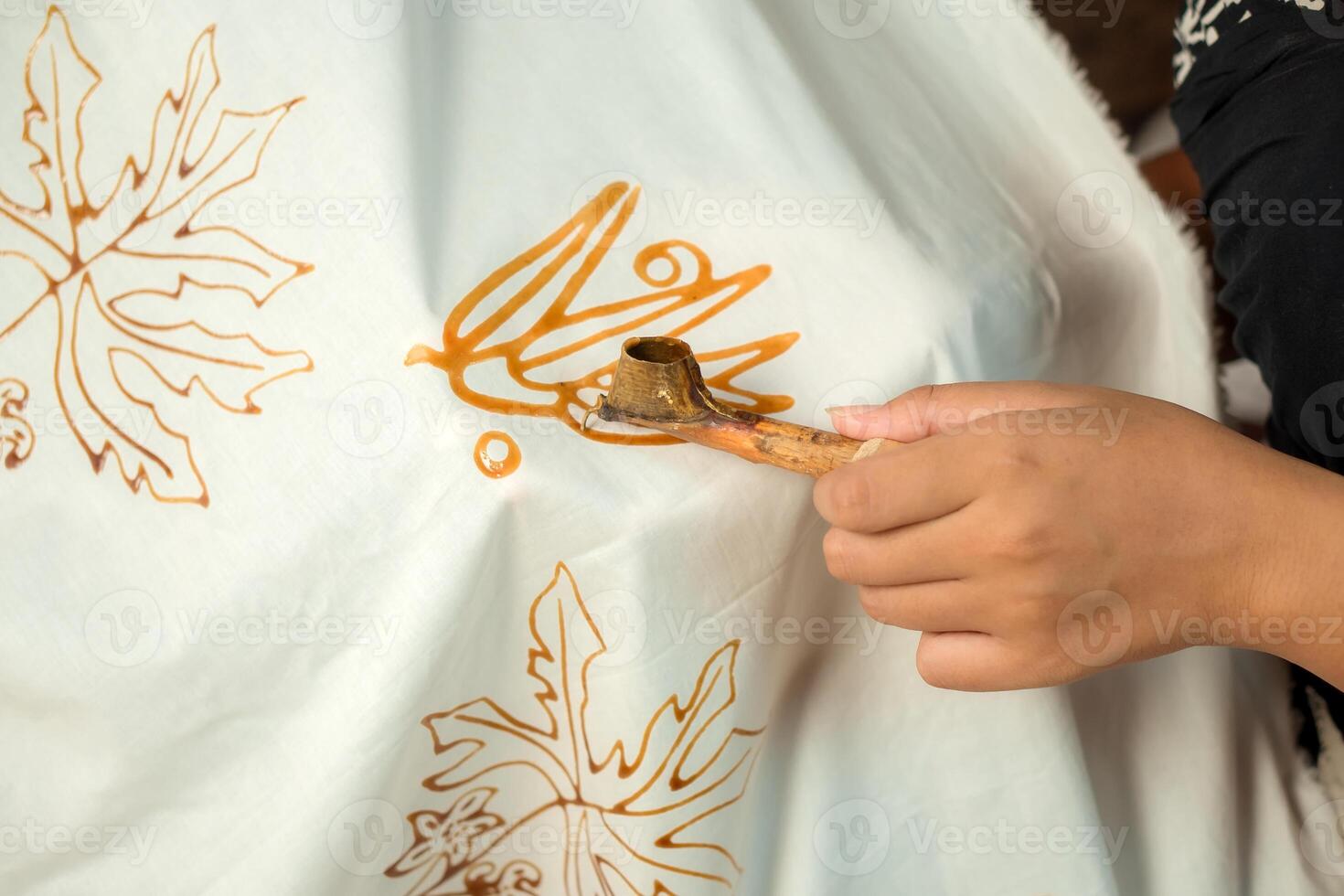 Close up an Indonesian woman focuses on applying intricate batik designs with a canting tool, creating beautiful patterns on fabric, showcasing traditional craftsmanship and skill photo