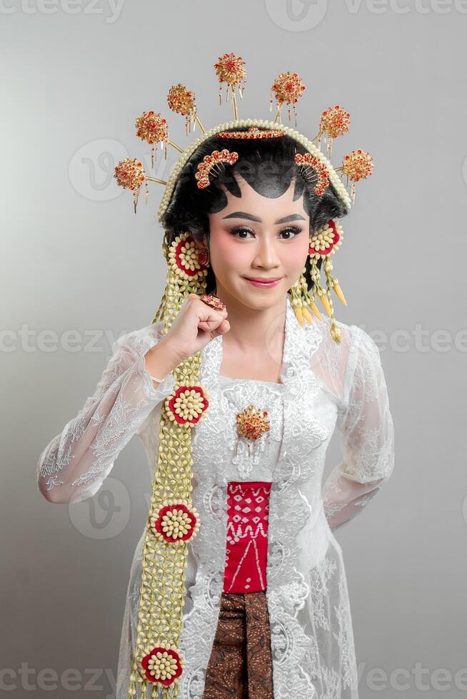 A Indonesian bride in Solo Putri attire, wearing a golden headdress and jasmine garland. She poses with a gentle smile and a raised fist, symbolizing confidence, elegance, and cultural pride. photo