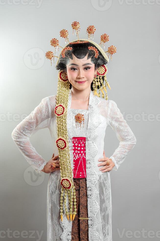 An Indonesian bride in Solo Putri attire, wearing a golden jasmine headdress, white lace kebaya, and batik. She smiles warmly with confidence, showcasing Javanese cultural elegance. photo