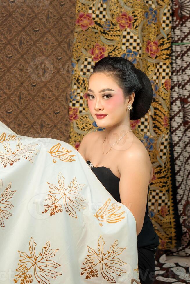 Indonesian woman poses with batik fabric, showcasing her intricate design work with delicate patterns, representing traditional craftsmanship and cultural artistry. photo