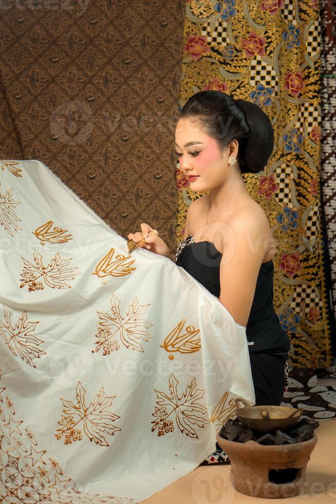 an Indonesian woman creating batik with a canting, wearing traditional attire. Elegant look, rich cultural heritage, and intricate patterns. Artistic craftsmanship of Southeast Asian textile art. photo