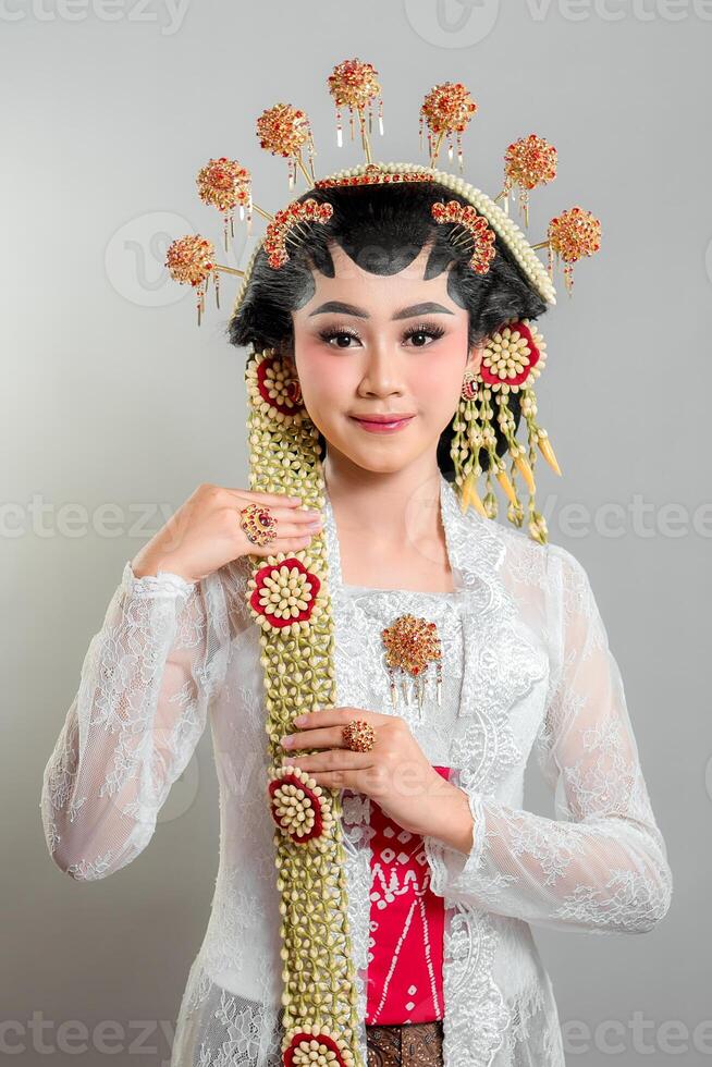 Indonesian bride in Solo Putri attire, wearing a golden headdress, jasmine garlands, and intricate lace kebaya. She exudes grace and elegance with a soft, charming smile. photo