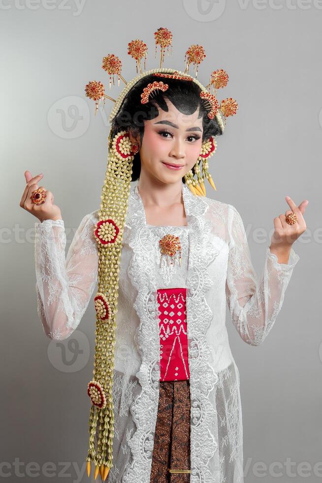 A elegant Indonesian bride in traditional Solo Putri attire, wearing a lace kebaya, intricate golden accessories, and jasmine garlands, smiling gracefully. photo