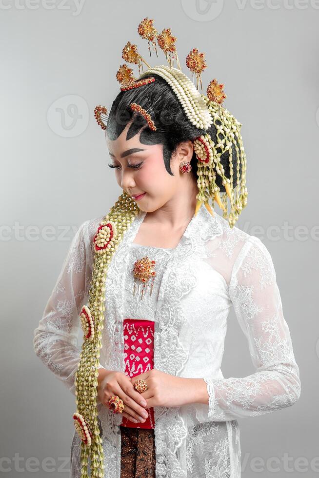 Elegant Indonesian bride in Solo Putri traditional attire, wearing a golden headdress, jasmine garlands, and intricate lace kebaya, radiating grace with a warm smile. photo