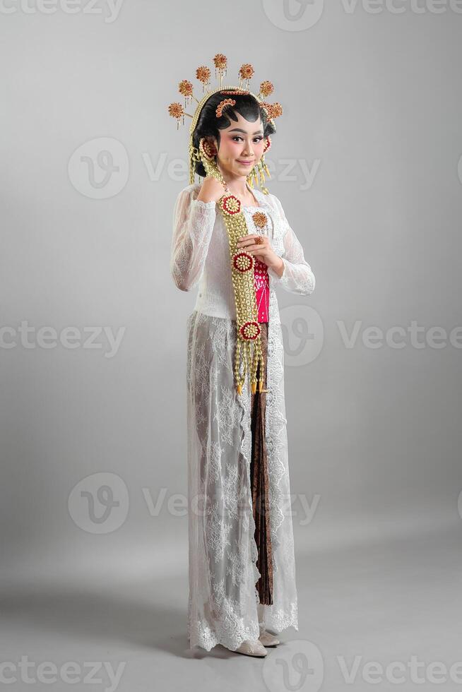 Indonesian bride in Solo Putri traditional attire, wearing an intricate golden headdress, jasmine garlands, and a white lace kebaya. She exudes elegance with a soft, graceful smile. photo