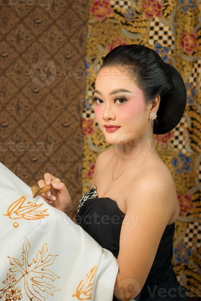 Indonesian woman creating batik with a canting, wearing traditional attire. Elegant look, rich cultural heritage and intricate patterns. Artistic craftsmanship of Southeast Asian textile art. photo