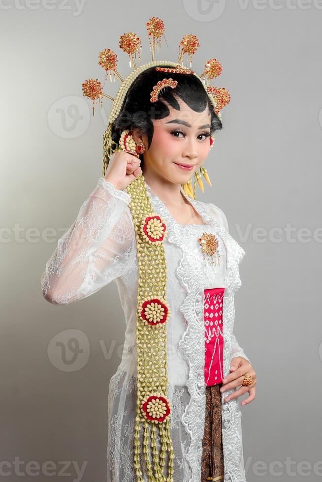 Indonesian bride in Solo Putri attire, wearing a golden headdress and jasmine garland. She poses with a soft smile and confident gesture, radiating elegance and tradition. photo