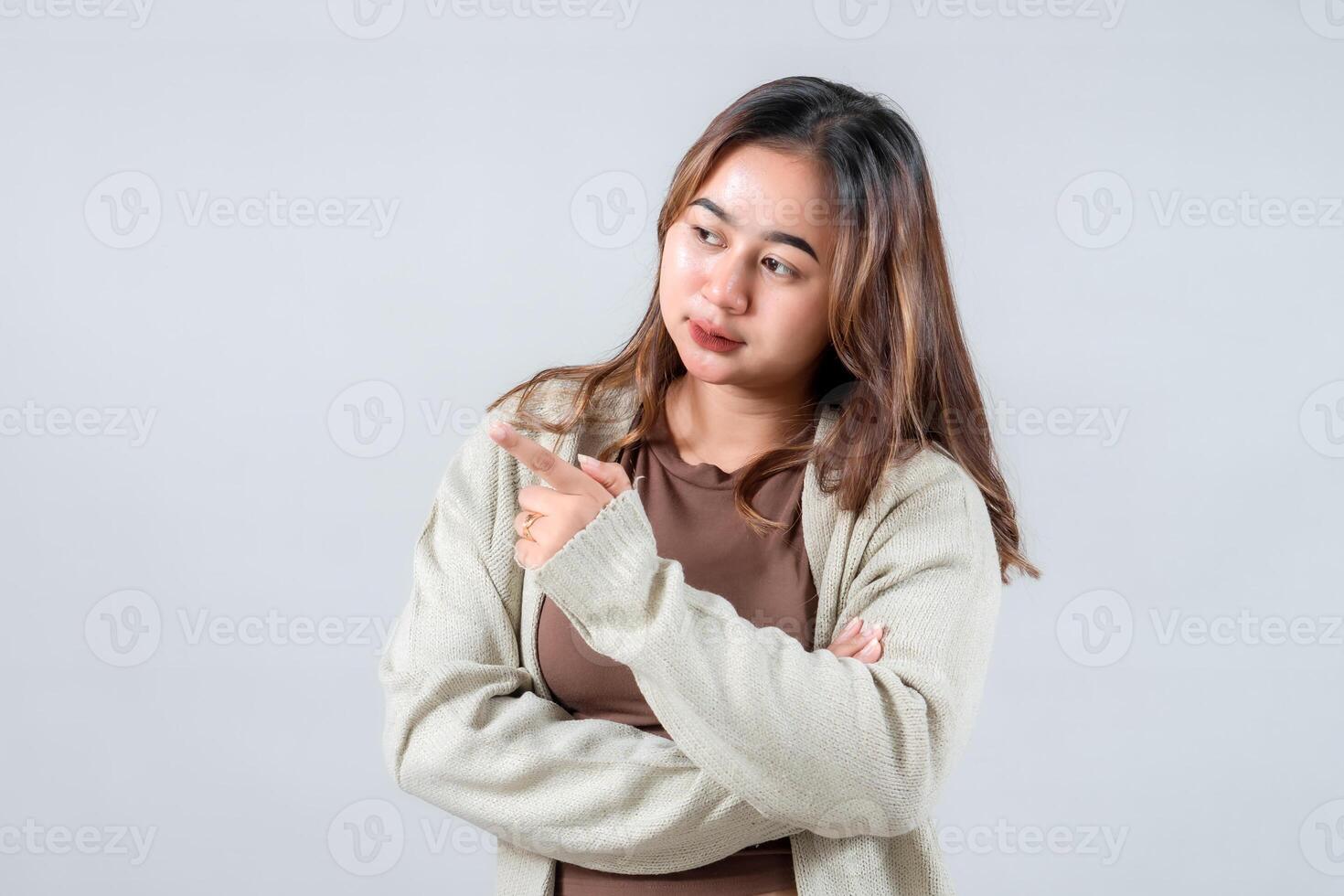 A young woman smiles brightly while pointing to the side, presenting something interesting. Her casual style and engaging expression make this image ideal for lifestyle and promotional projects. photo