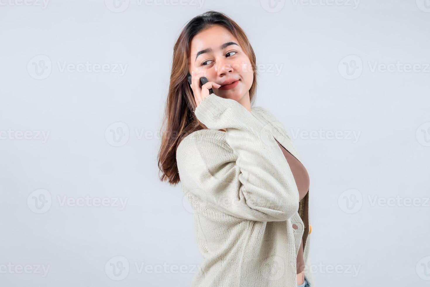 A young woman in a cozy sweater smiles while talking on her mobile phone, conveying connection and communication against a neutral background photo