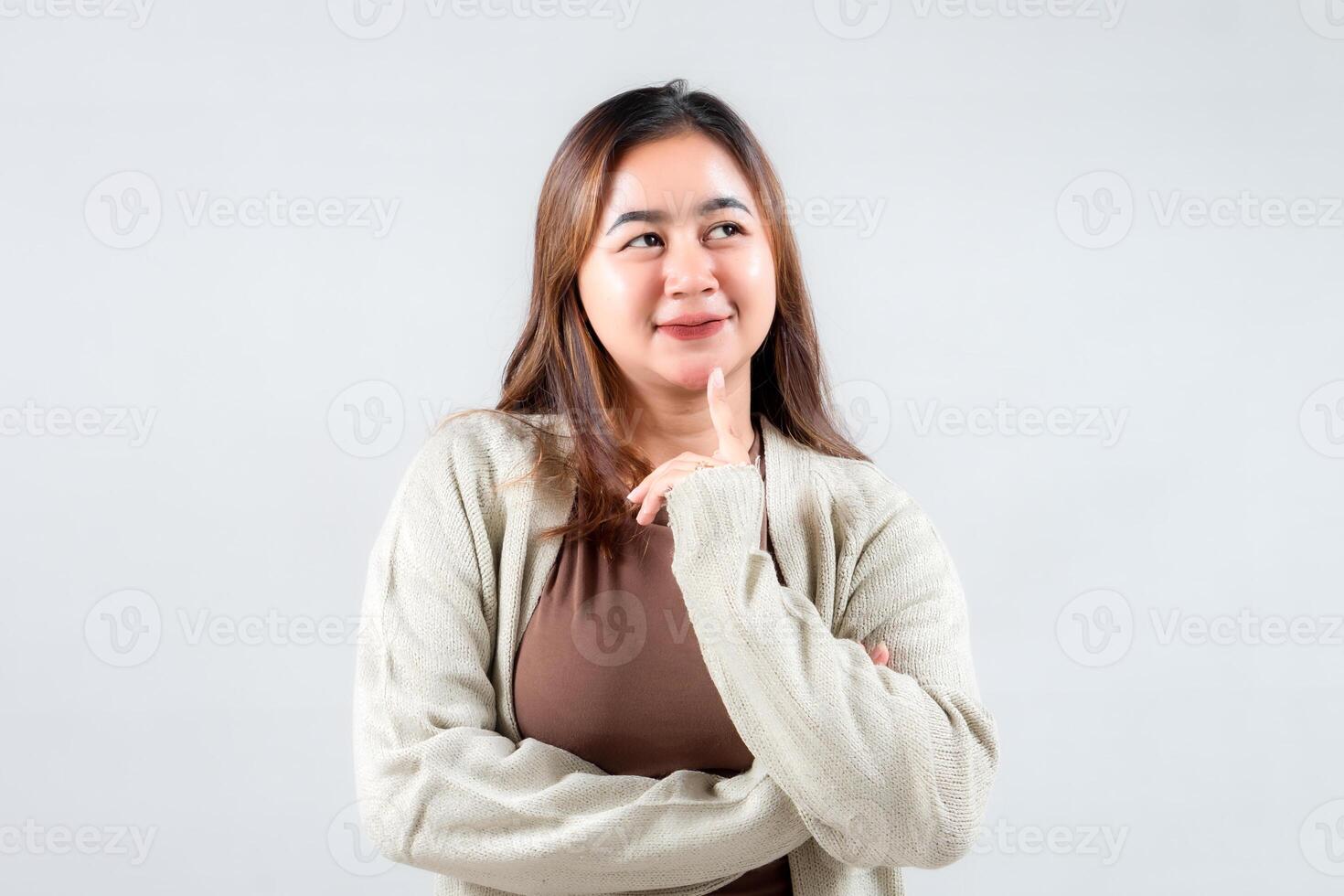 A thoughtful young woman poses with a finger on her lips, conveying a sense of curiosity and intrigue. Her casual outfit and expressive look make this image ideal for lifestyle and creative projects. photo