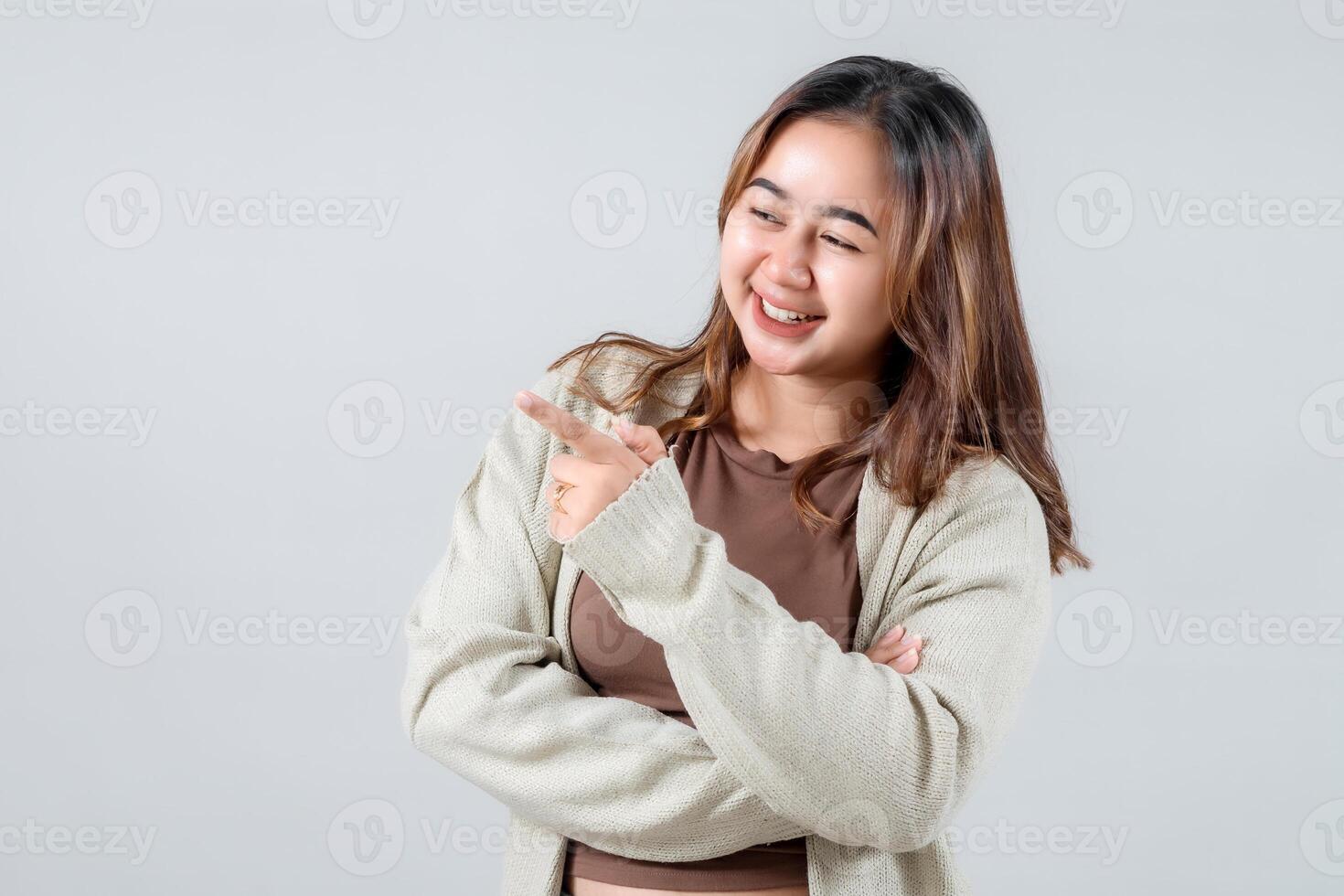 A young woman smiles brightly while pointing to the side, presenting something interesting. Her casual style and engaging expression make this image ideal for lifestyle and promotional projects photo