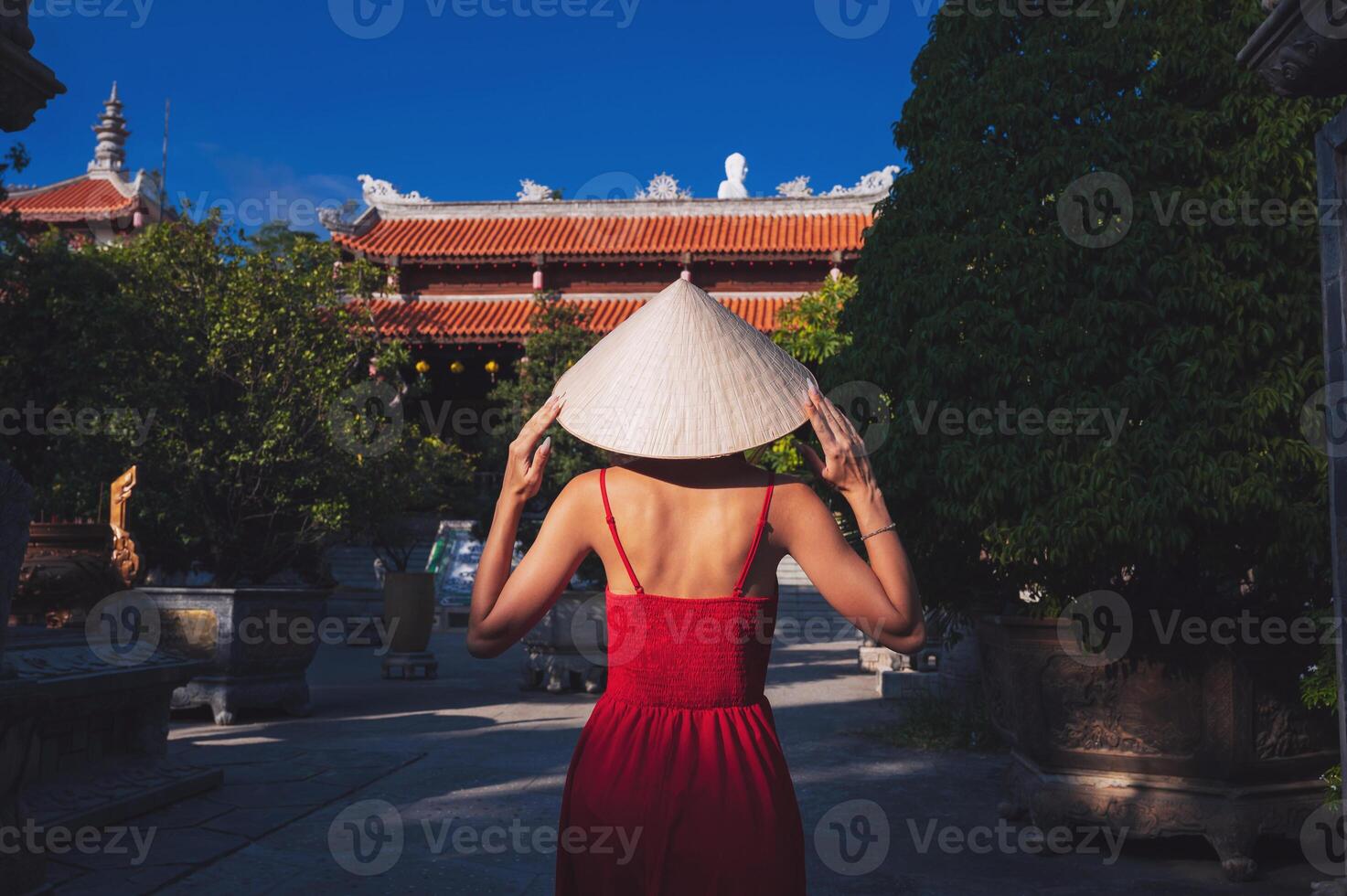 back of beautiful female traveler in a dress and a traditional Vietnamese hat Non La at a pagoda in Vietnam on a travel to Asia photo