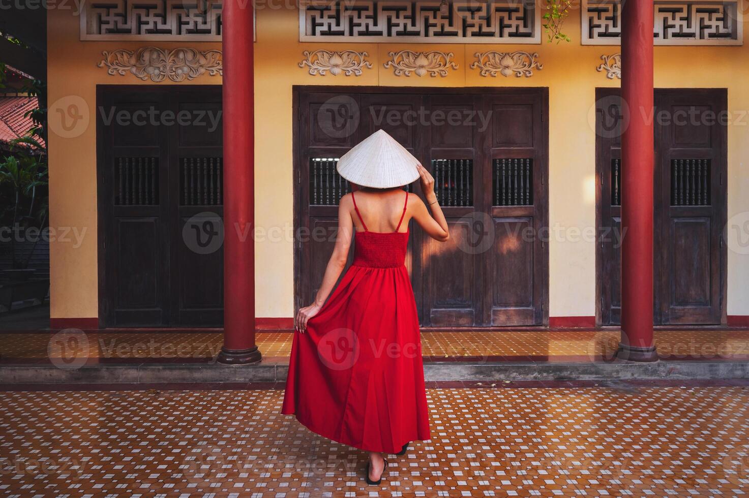 back of a beautiful woman traveler in a dress and a traditional Vietnamese hat at pagoda in Vietnam on a travel to Asia photo