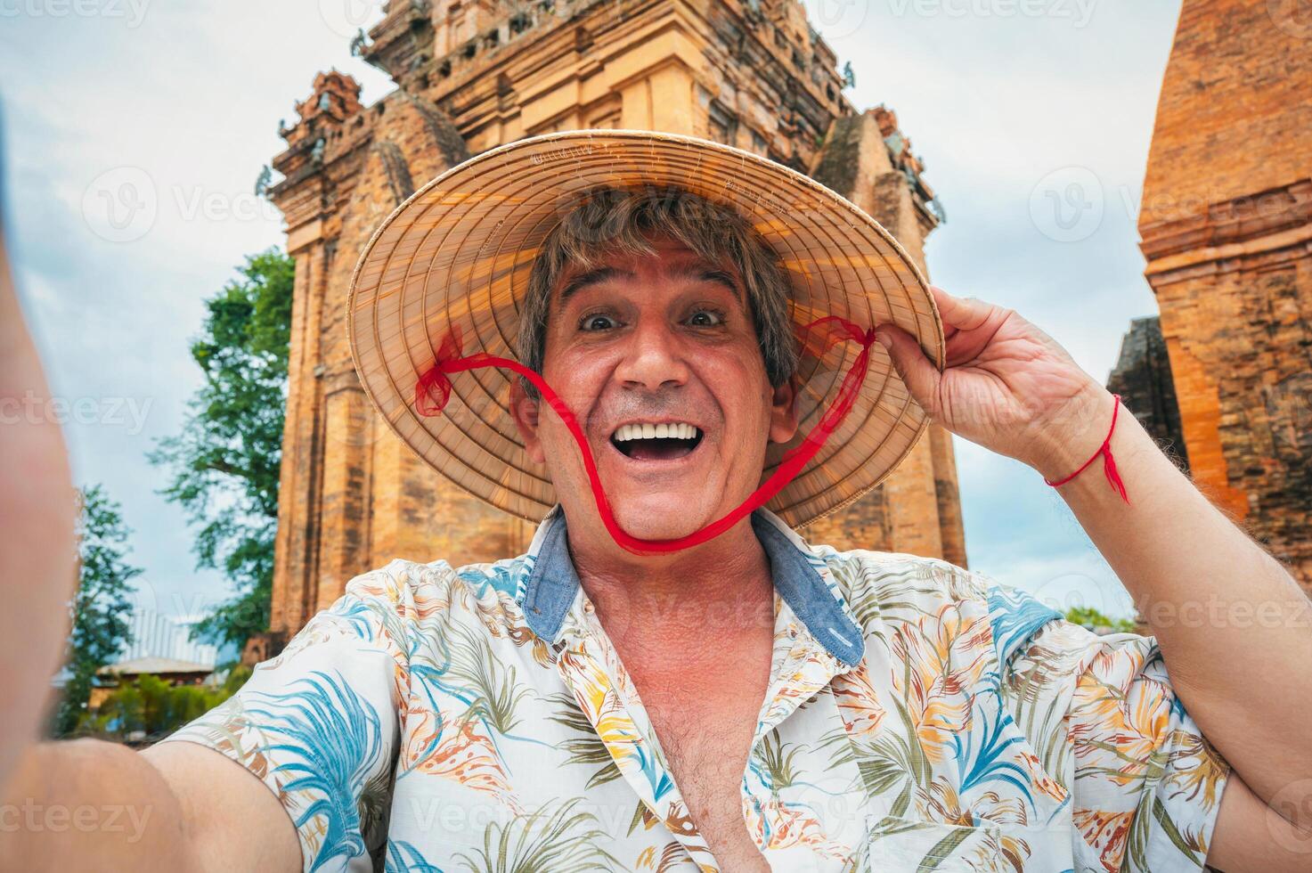 happy elderly male traveler in Vietnamese cone hat non la takes a selfie at Po Nagar Cham Towers in Nha Trang, Vietnam. The concept of travel in Asia photo