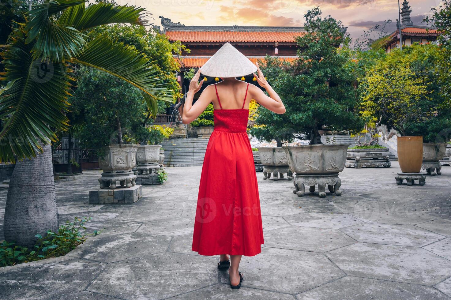 back of a female tourist traveler in a Vietnamese hat and red dress at Long Son Buddhist Pagoda in Nha Trang in Vietnam. Travel and tourism in Asia photo
