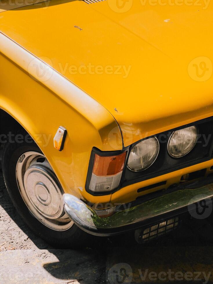 Close up view of vibrant yellow vintage car parked on sunny day, highlighting its classic design, chrome details, and nostalgic appeal, evoking sense of timeless automotive beauty. Vintage yellow car photo