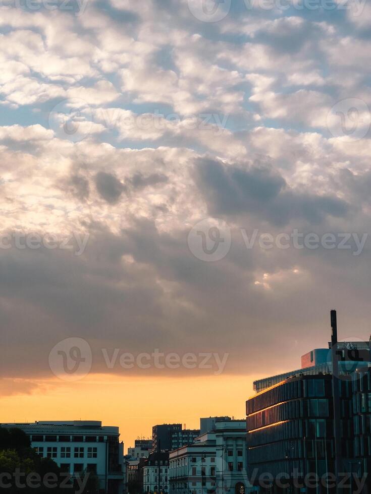 Skyline reflecting orange sunset light under cloudy sky with modern and historical buildings at golden hour in city. Cityscape glows with warm sunset, blending contemporary and historic architecture photo