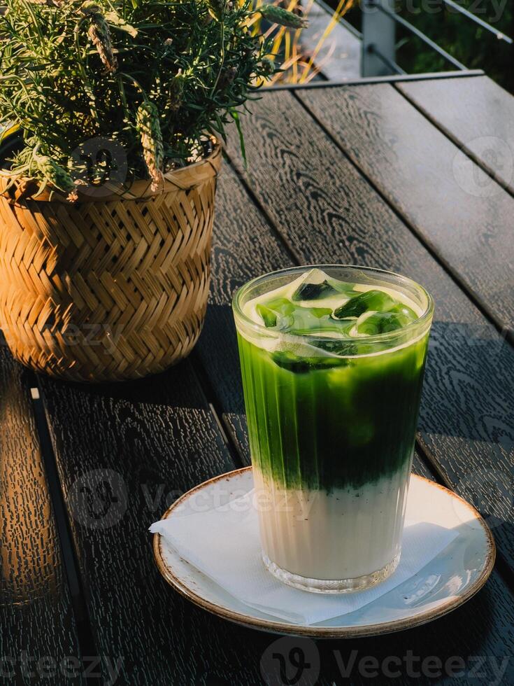 Cold matcha latte in tall glass with a smooth blend of green tea and milk. healthy drink offers refreshing taste and organic ingredients. glass of iced matcha latte in warm sunlight, outdoor setting photo
