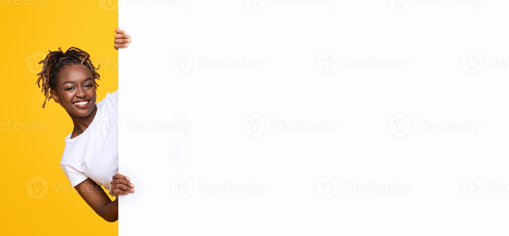 Smiling african american girl with white empty board for advertisement over yellow studio background, panorama photo