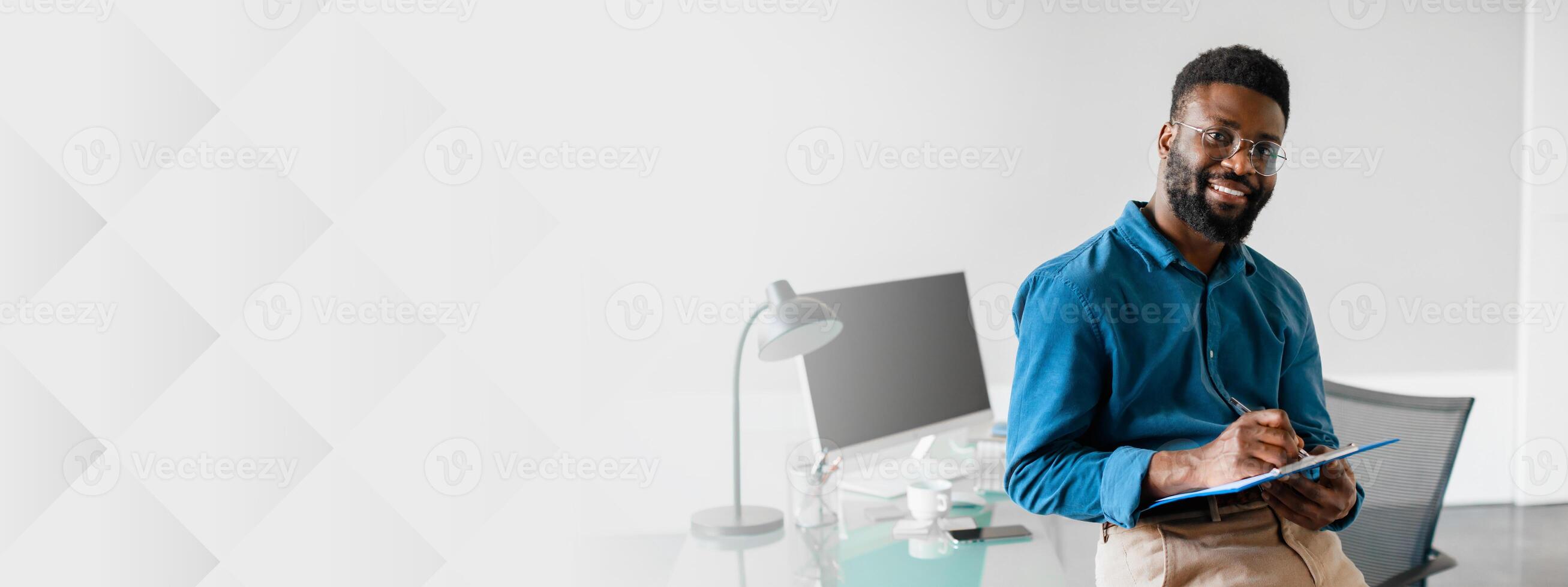 A young African American businessman sits in a contemporary office, confidently taking notes on a clipboard. He embodies the spirit of entrepreneurship while preparing for future opportunities. photo