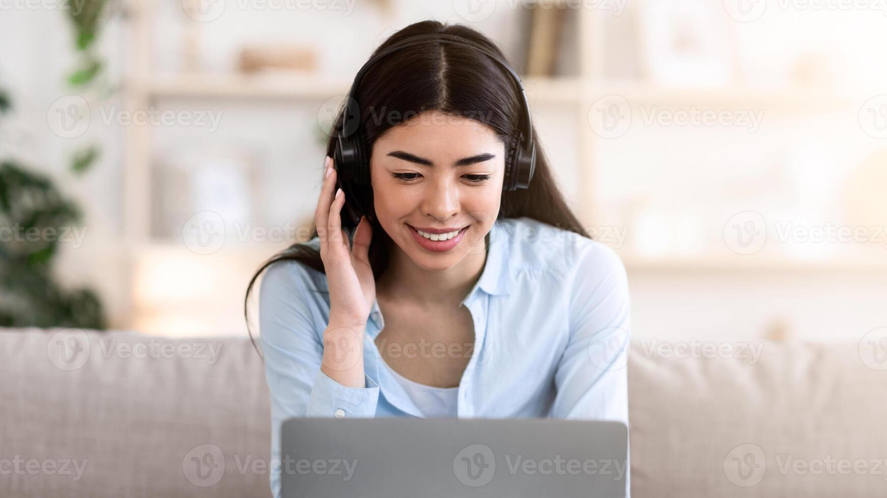 Webinar. Smiling asian girl studying online with laptop and headset at home, sitting on sofa in living room, copy space photo