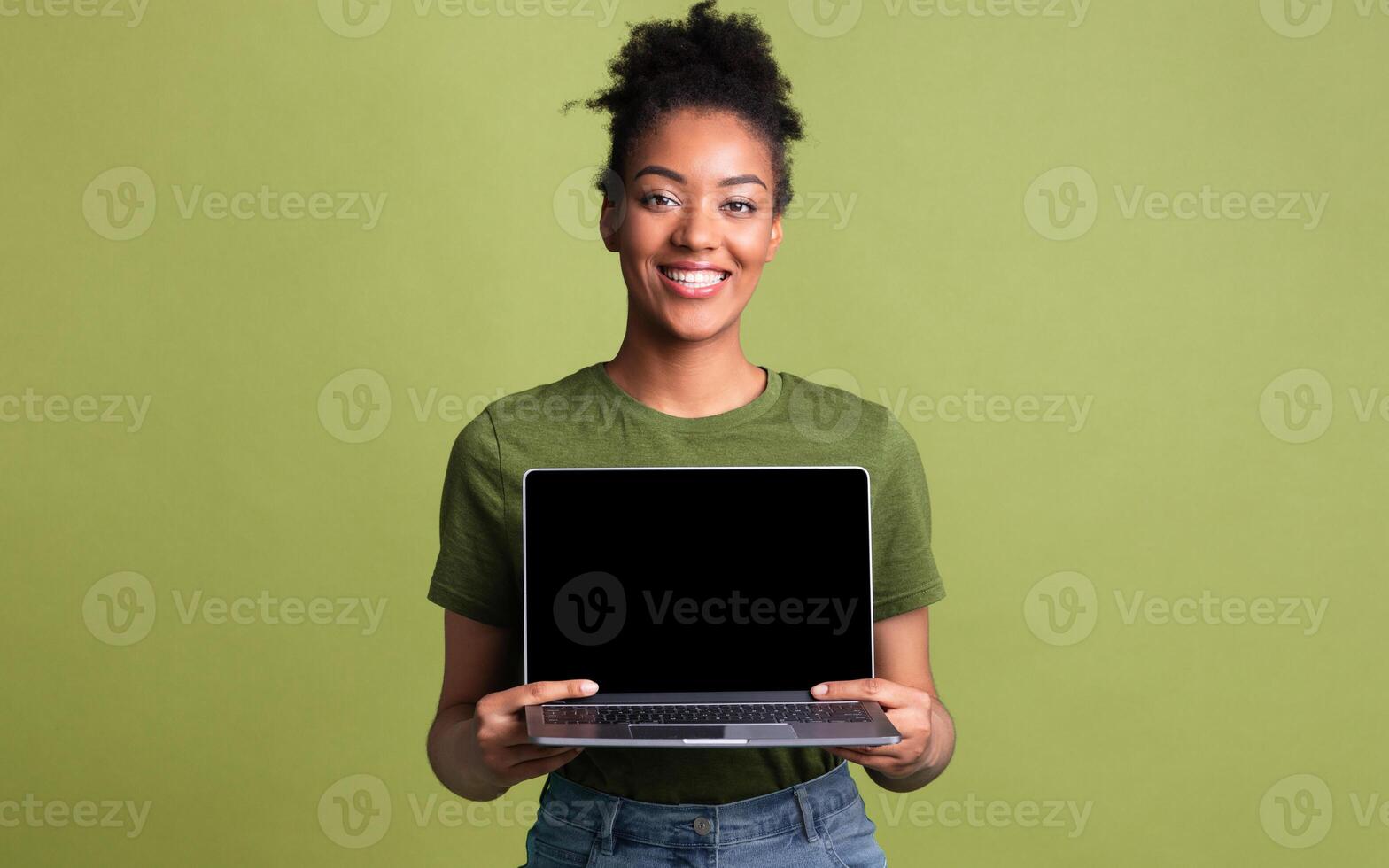 Useful Website. Cheerful afro girl holding laptop computer, showing blank screen over green studio wall, mock up photo