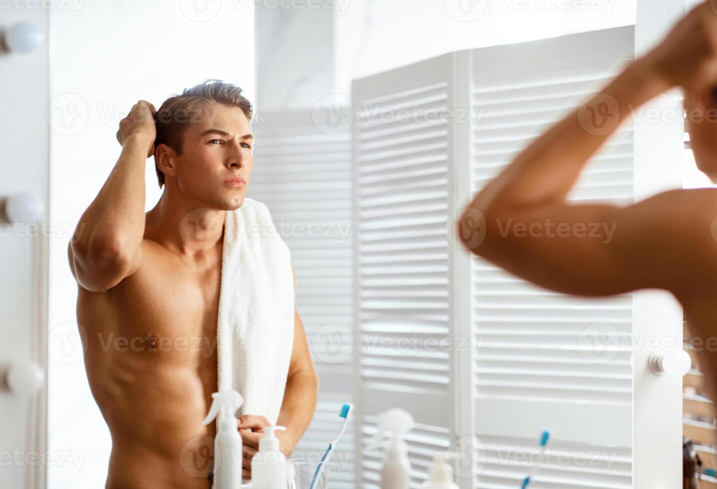 Focused man looking in mirror putting wax touching his hair styling or checking for hair loss problem photo