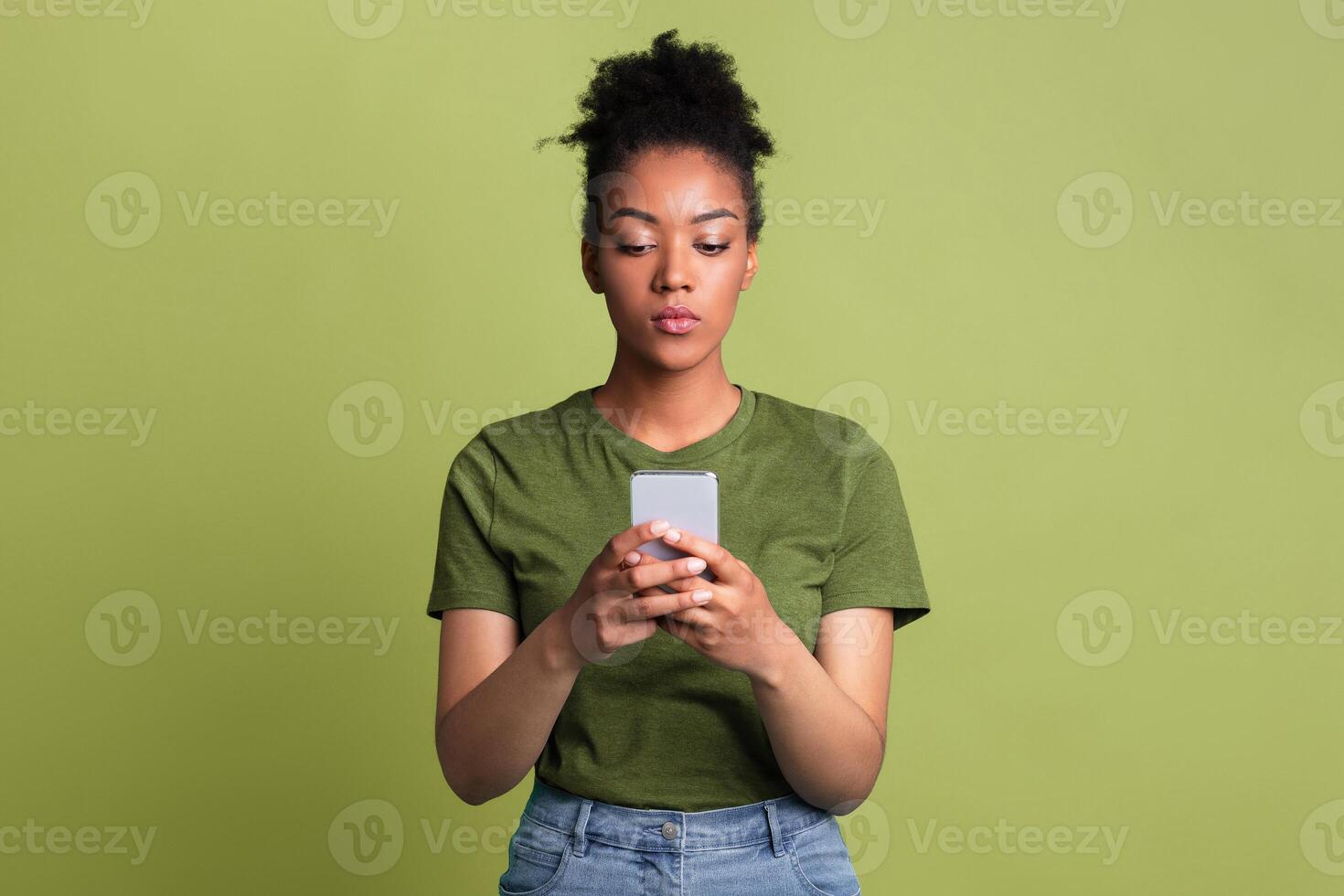 Gadget Addiction Concept. Portrait of serious black girl using cell phone on green studio background photo