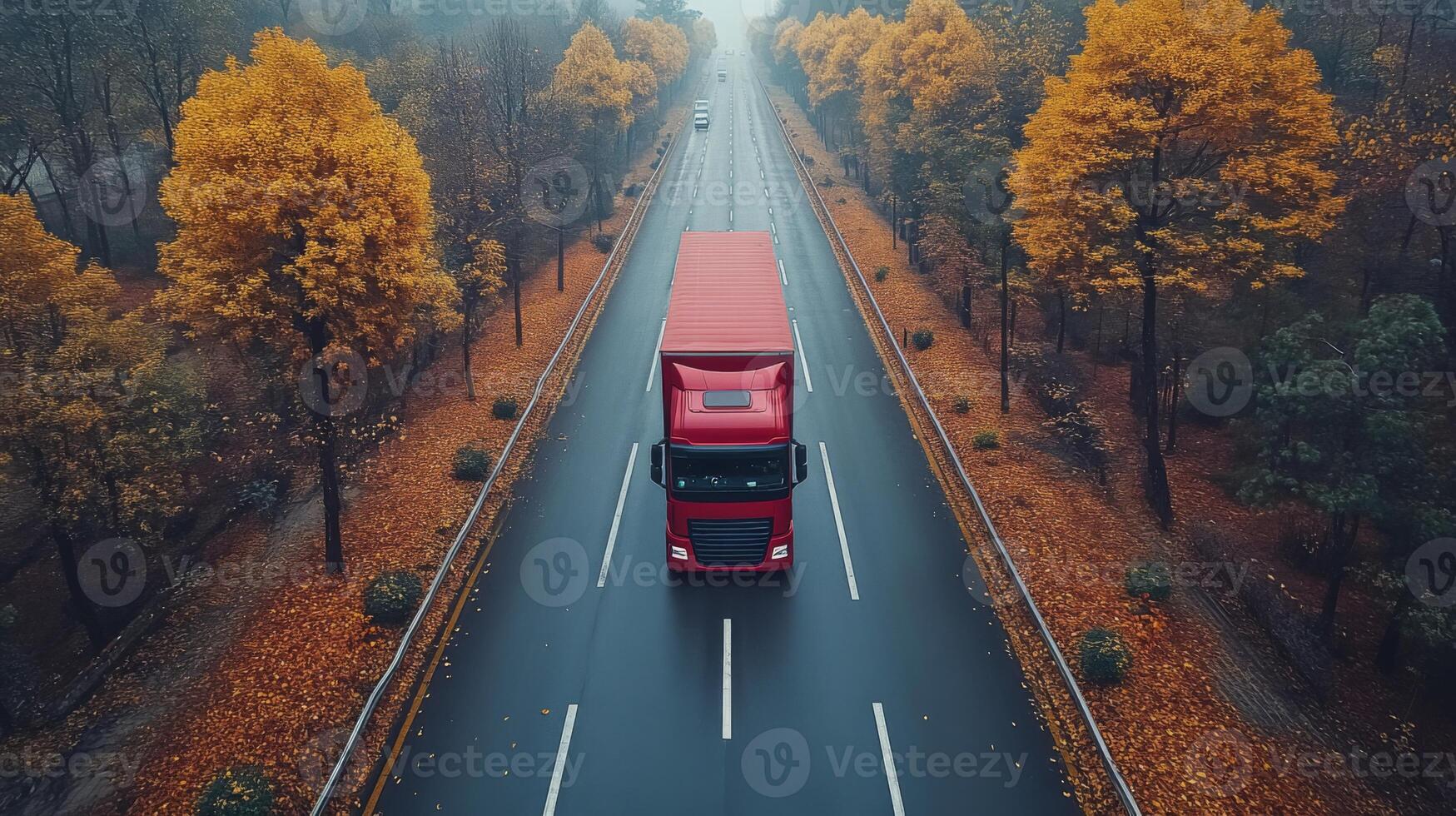 A red truck drives on a wet road lined with vibrant autumn trees, efficiently transporting goods through a scenic logistics route in overcast weather. photo