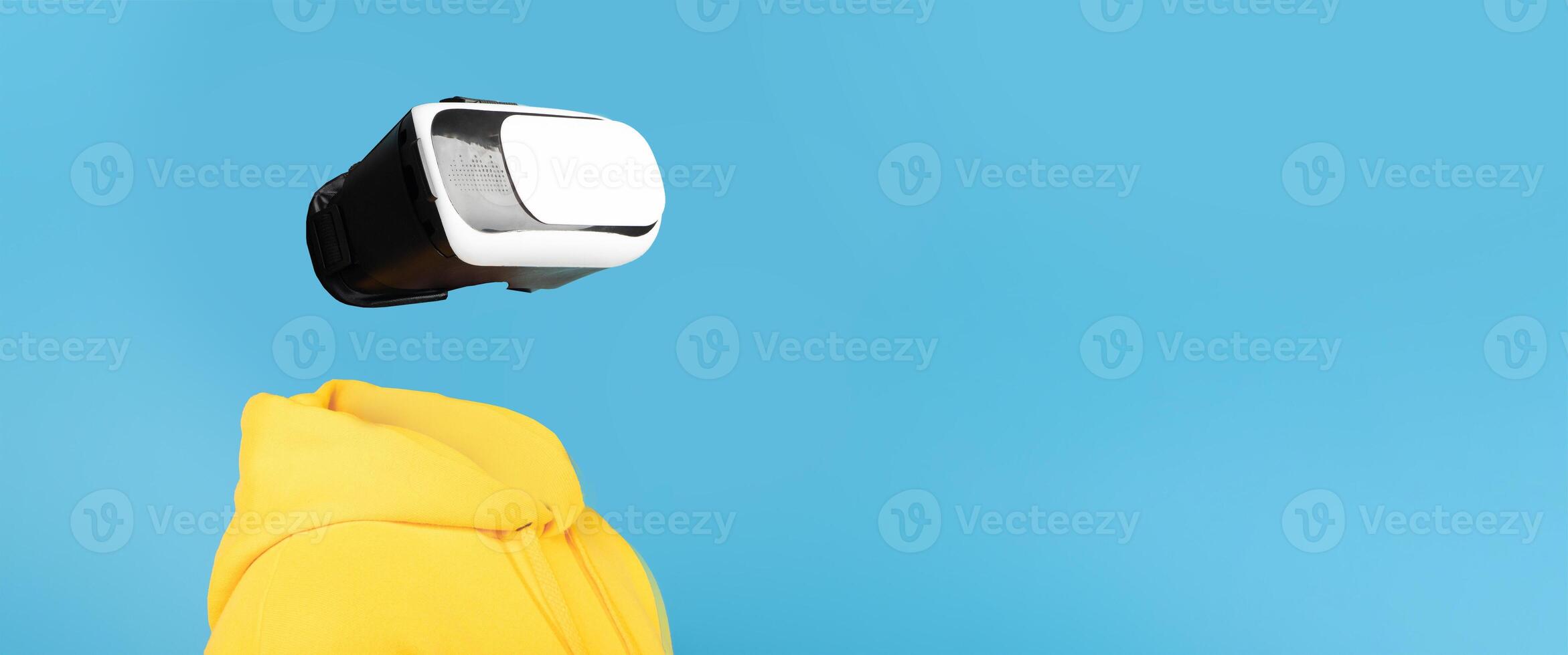 A person wearing a VR headset engages with virtual reality technology. The isolated background highlights the futuristic gadget and the user's bright yellow hoodie, creating an imaginative setting. photo