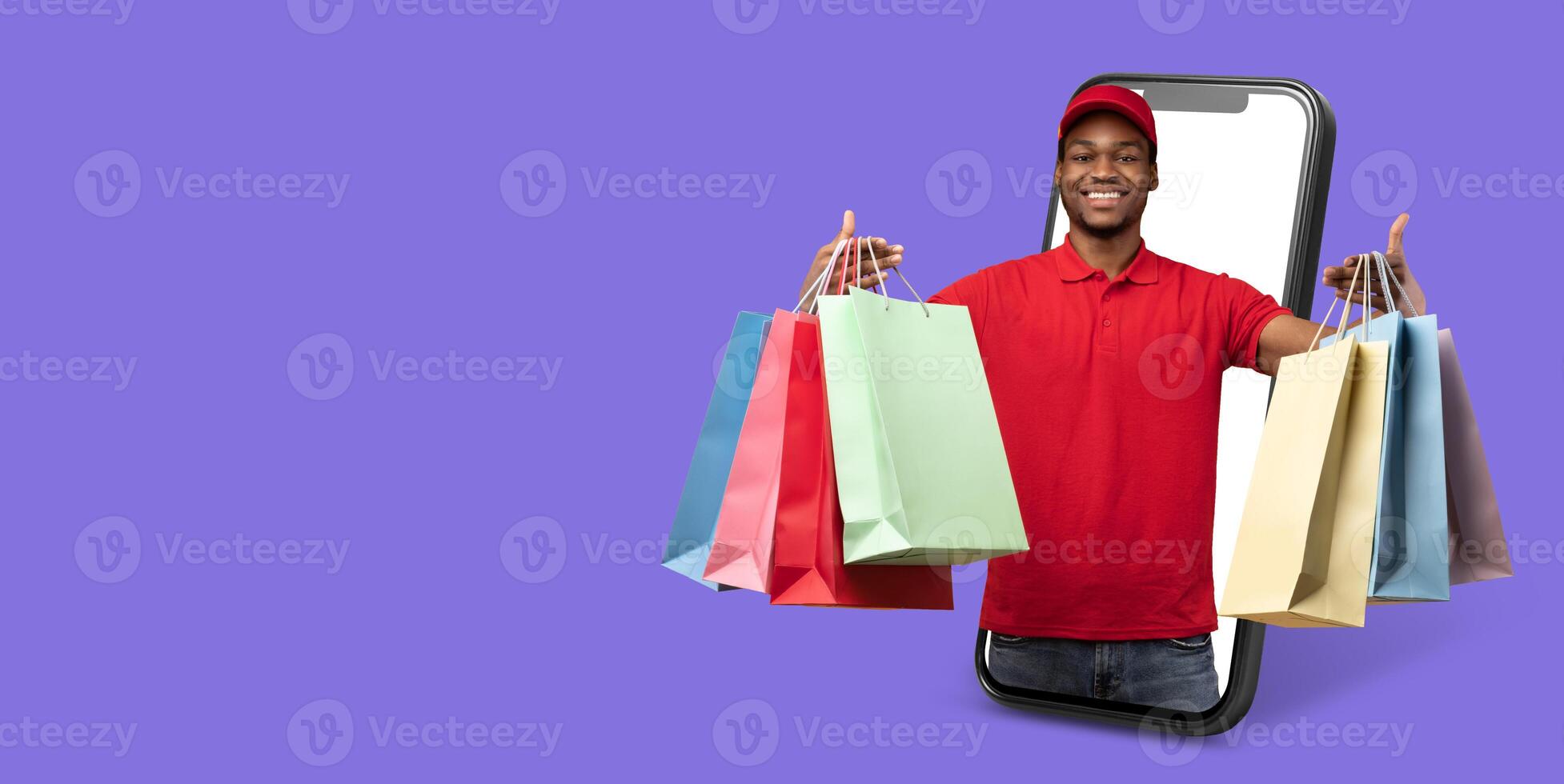 A cheerful delivery man holds several shopping bags while interacting with a smartphone. This showcases the convenience of online shopping on a large screen, emphasizing modern commerce. photo