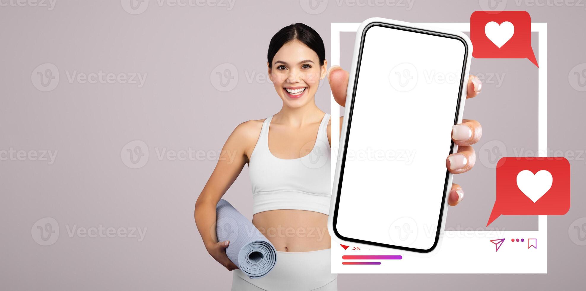 A cheerful influencer stands against a neutral backdrop, showcasing a blank smartphone while holding a yoga mat. Social media icons appear alongside her, suggesting online interaction and connection. photo