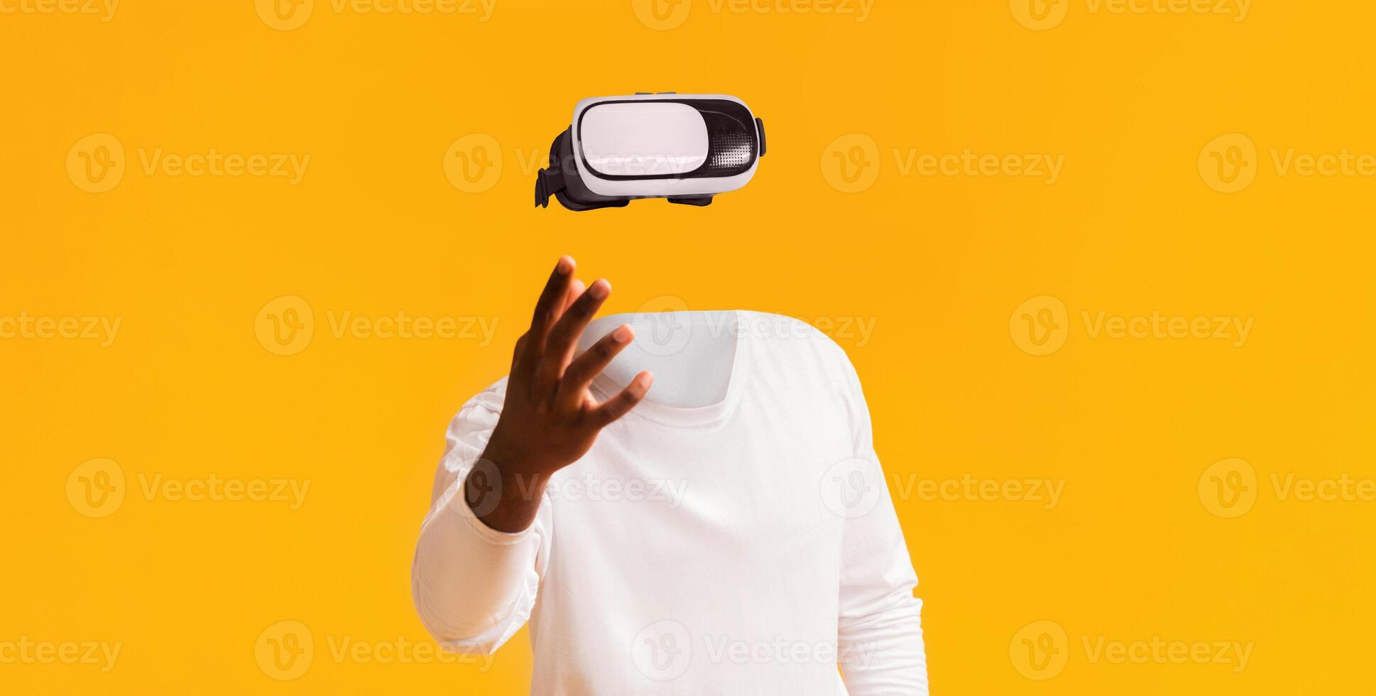 A user engages with virtual reality technology, wearing futuristic goggles and extending their hand. The vibrant yellow background enhances the modern, immersive experience. photo