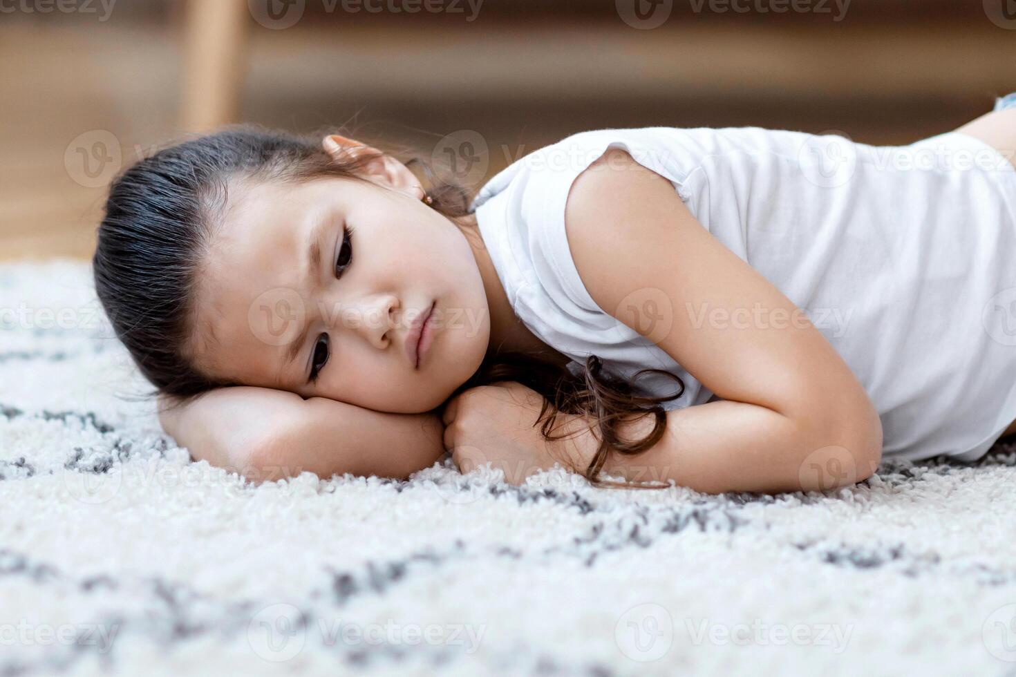 Depressed Asian Kid Girl Lying On Floor Feeling Lonely And Unhappy At Home. Loneliness Concept photo